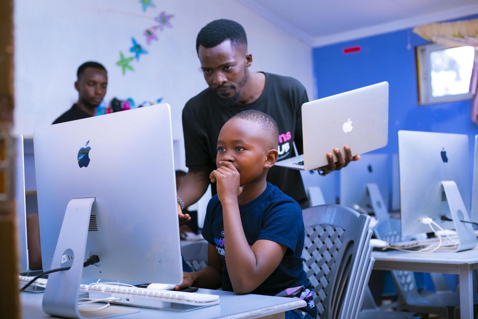 An instructor with a laptop guiding a learner at an iMac