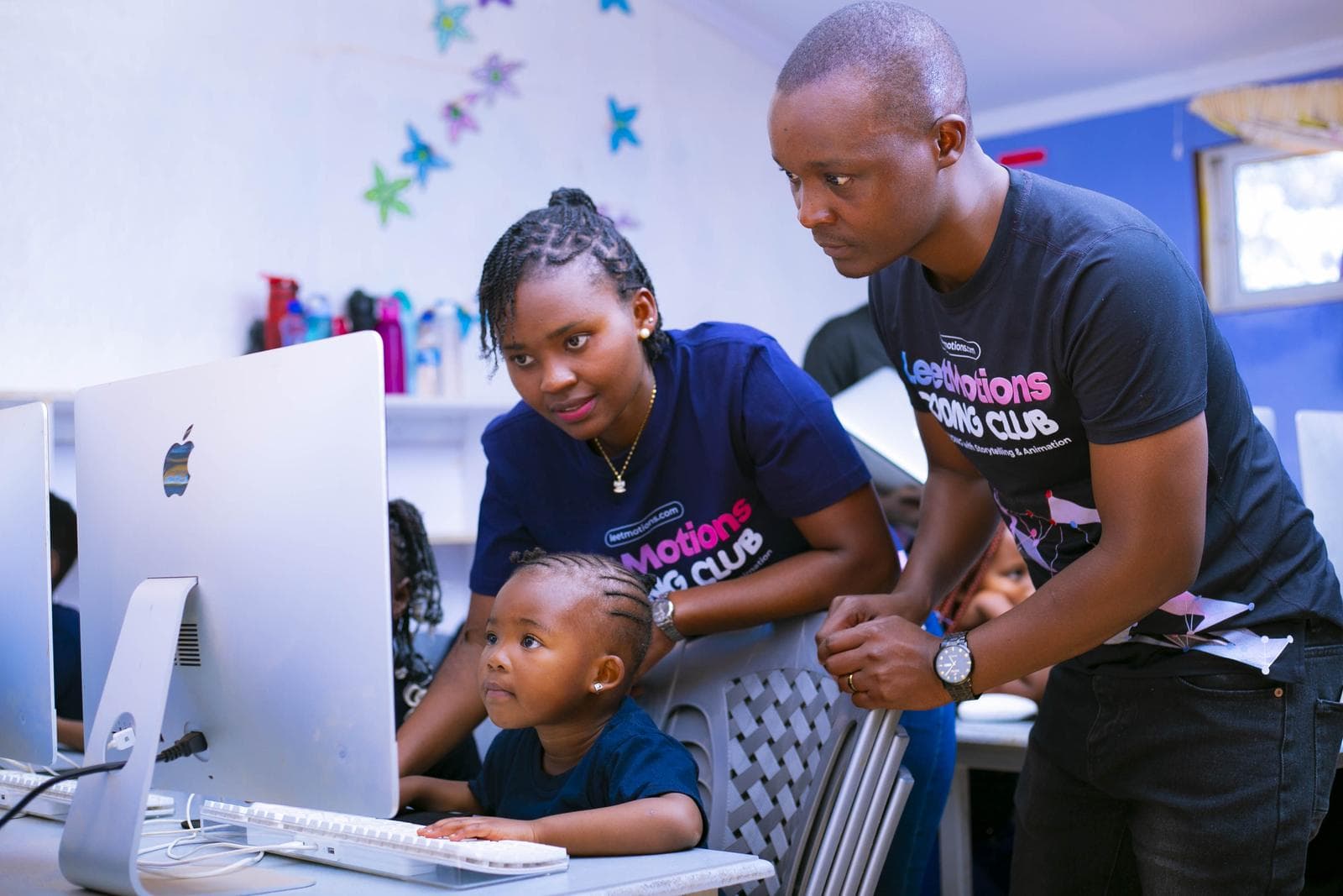 Two instructors guiding one of the youngest learners at an iMac