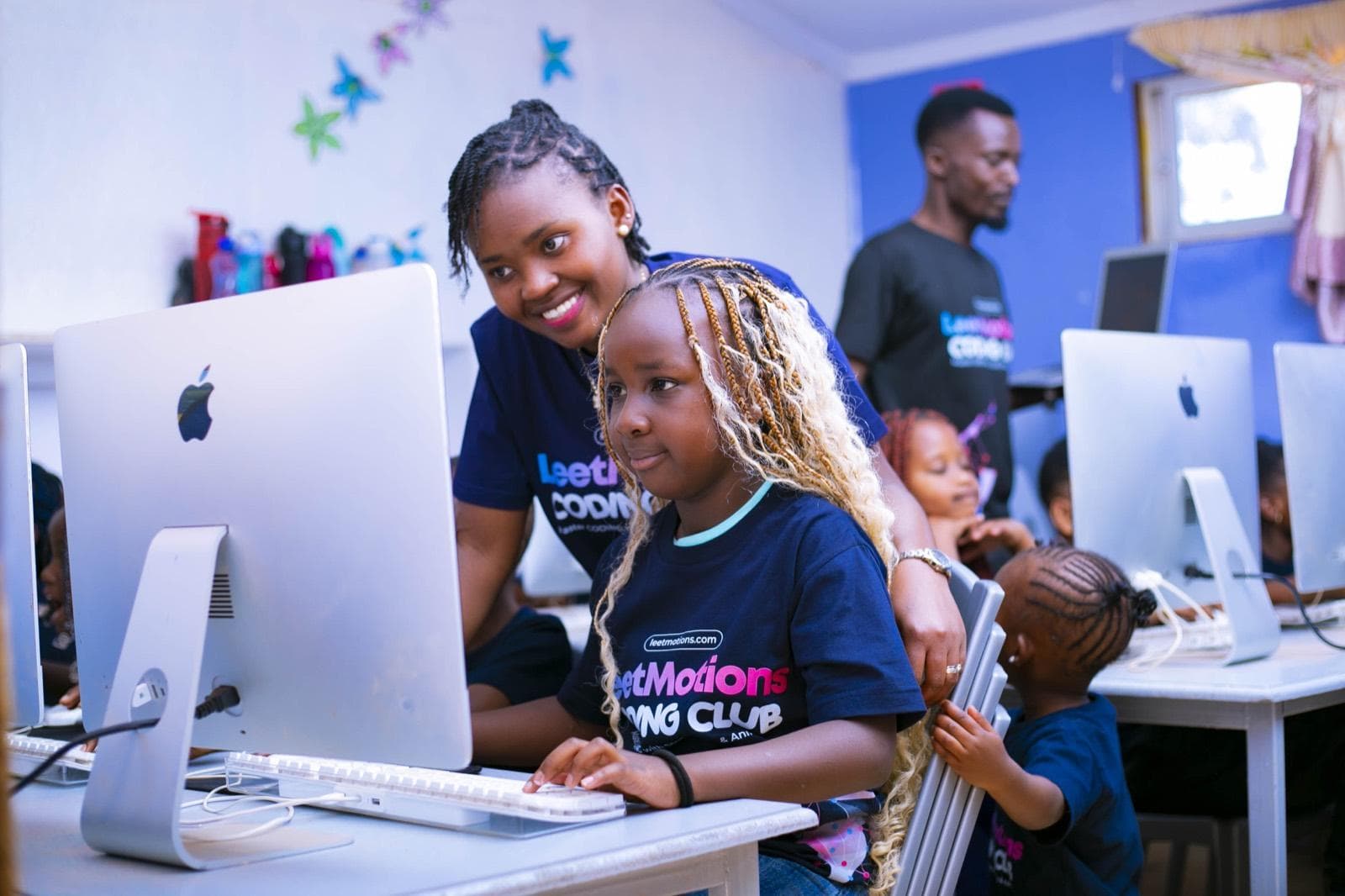 A LeetMotions instructor smiling beside a young learner coding on an iMac